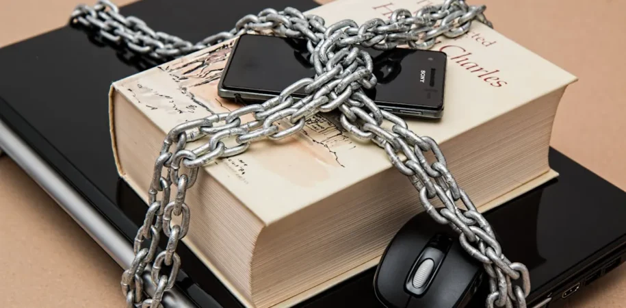Laptop, book, phone, and mouse chained together to symbolize cybersecurity