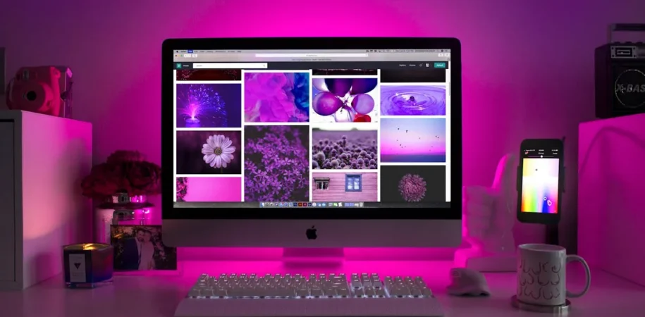Desktop computer with pink background showing website designs on screen
