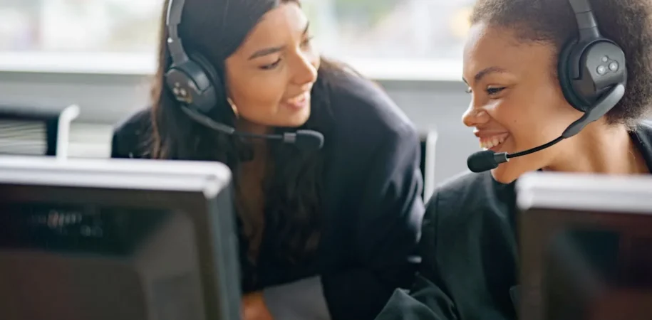 Two female support agents with headsets talking at their computers